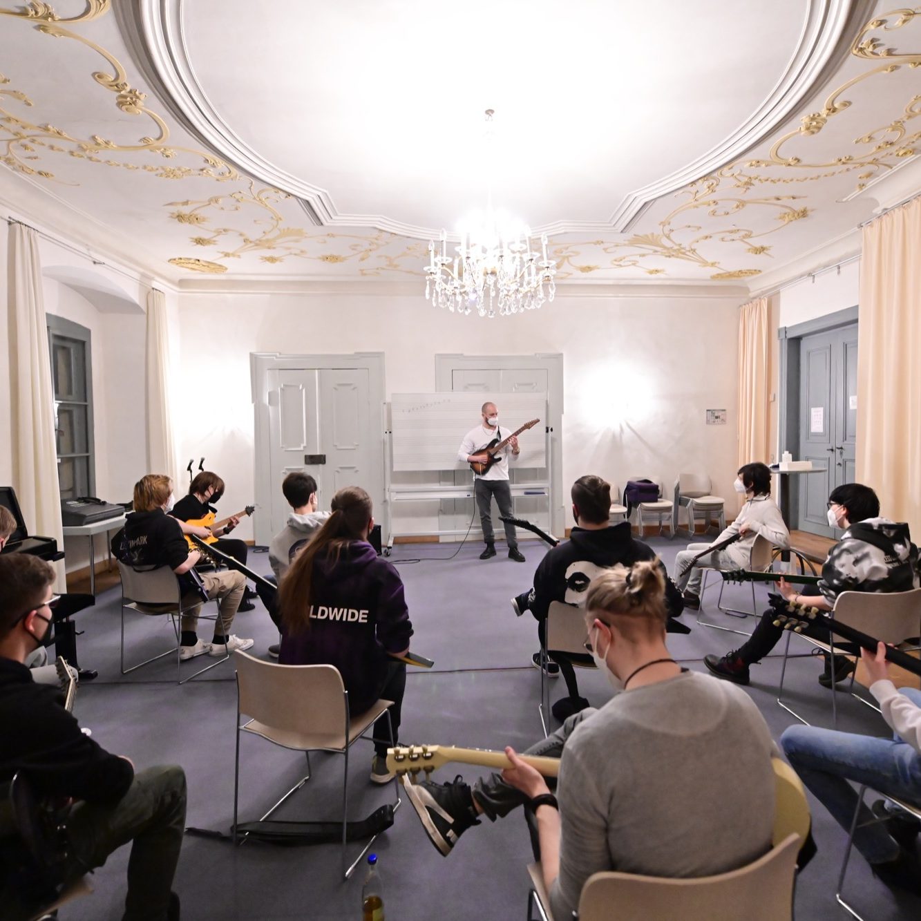 Team building musik gitarre Tobias Mertens Eine Gruppe von Musikern sitzt im Kreis und beobachtet einen Gitarrenunterricht.